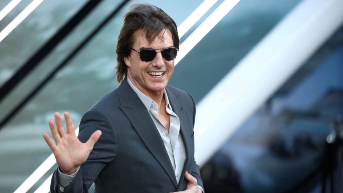 Adam Sandler sonriendo en un evento, vestido con un traje informal.